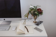 desk with notebook, computer, pencil, cellphone, books, and vase of flowers 