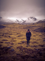a woman standing outdoors with distant snow capped mountains in the background 