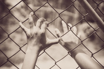 hands grasping to a chain link fence 