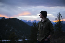 a man in a wool cap standing on a mountaintop at sunrise 