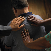 Hands laid on a man's back in prayer.