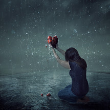 a woman on her knees holding a broken heart in the rain 