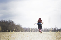 woman running through a field with open arms 