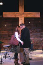 a couple holding hands praying in front of a cross 