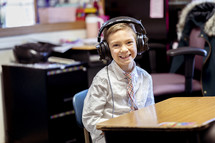 a boy sitting at a desk in a classroom wearing headphones 