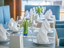 Interior design of a beautiful restaurant in a marine style. Table setting with glasses, plates, napkins and flowers