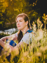 A woman sits in the grass looking  into the distance