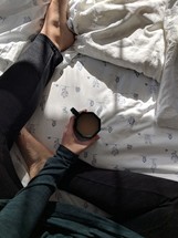 a woman sitting on a bed with a cup of coffee 