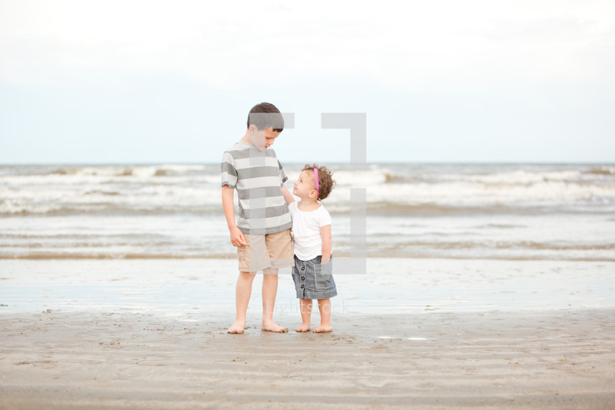 brother and sister standing in the sand on a beach 