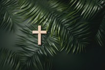 Wooden cross and palm leaves on dark green background, top view. Palm Sunday