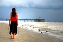 woman walking on a beach towards a pier 