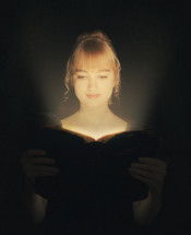 A woman's face glowing as she opens a Bible. 