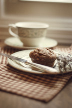 Muffin on a plate with tea and sage.