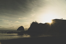 sunburst behind cliffs on a beach at sunset 