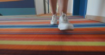 Close-up of white sneakers on multicolored rug walking in a hotel corridor - steadicam shot