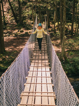 a woman walking across a swinging bridge 