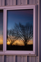 Reflection of trees and sunrise in windows of farm house