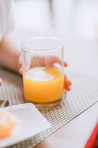 child's hand on a glass of orange juice 