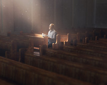 A man is alone in a church with glowing lights coming from above.