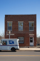 Post office truck in front of red brick building in small town