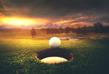 A golf ball rolls into a hole during sunset on a mountian course.