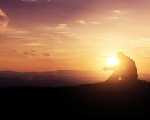 silhouette of a man praying at sunset 