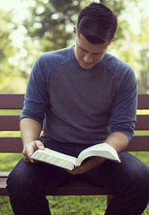 a man reading a Bible on a park bench 