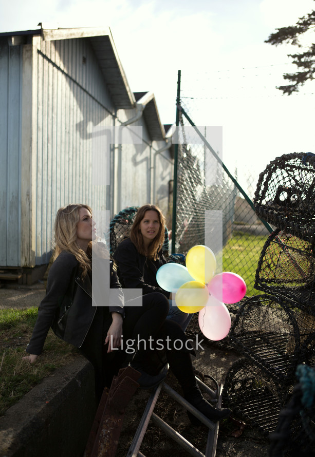 women with balloons sitting near crab cages outdoors 