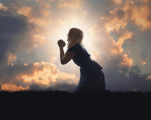 a woman kneeling in prayer at sunset 