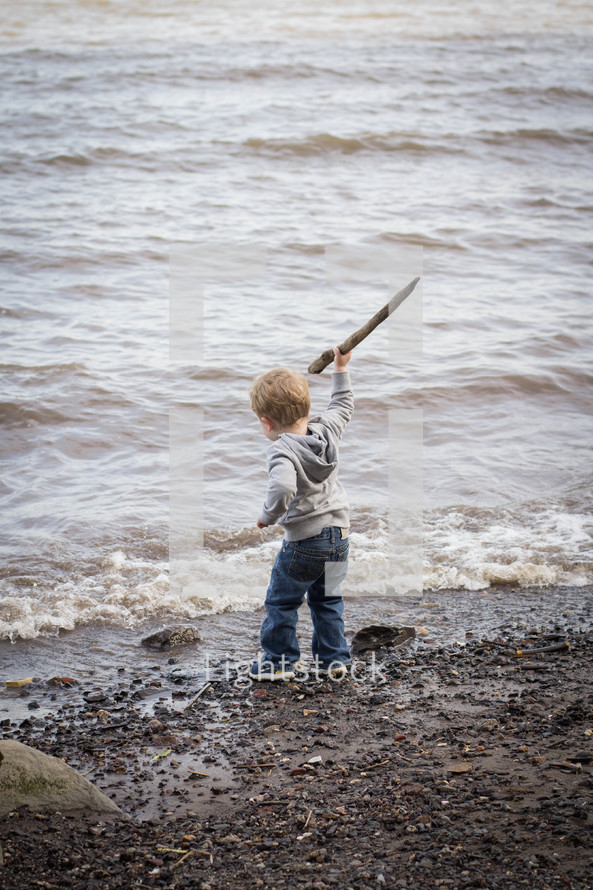 Boy holding a stick on the beach at the ocean.