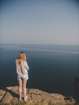 a woman standing at the edge of a cliff taking pictures of the water below 