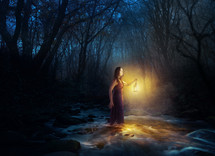 a woman carrying a lantern through a stream in a dark forest 