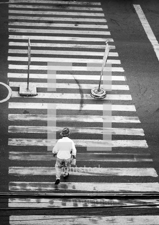 An elderly man crossing the street alone at a crosswalk
