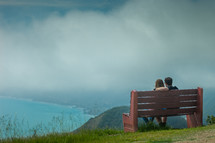 A couple sitting on a bench overlooking the Pacific Ocean in Big Sur.