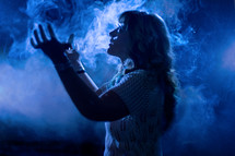 woman with raised hands standing in smoke 