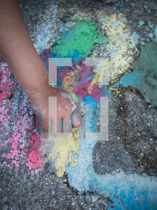 a child's hand draws on the pavement with colored chalk