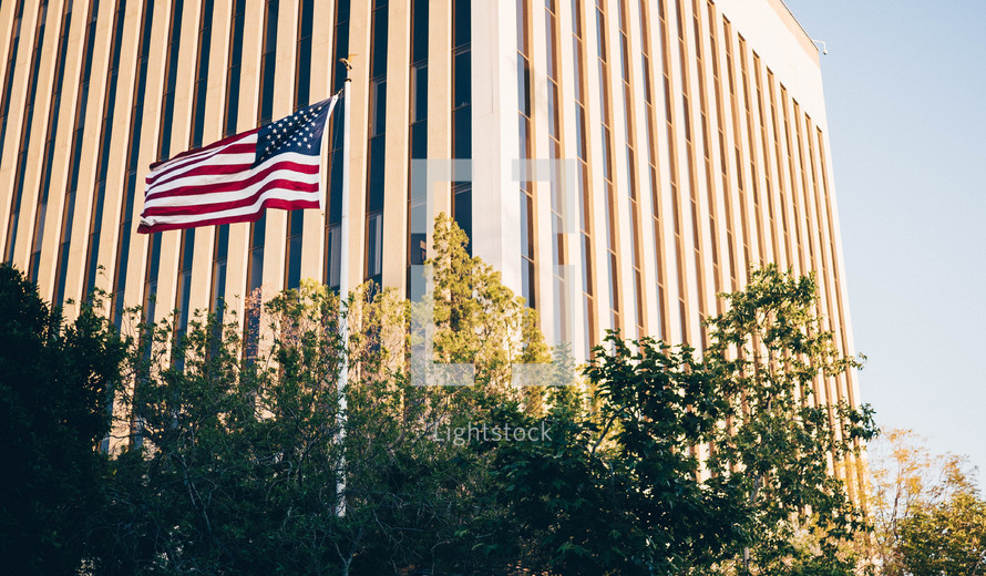 American flag on a flag pole and a tall building in the background 