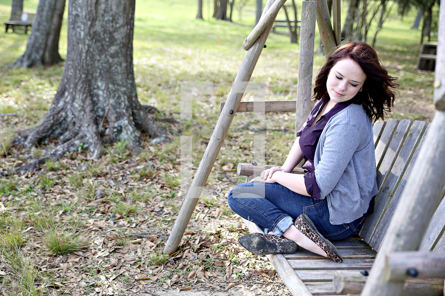 A young woman sitting outdoors on a wooden swing.