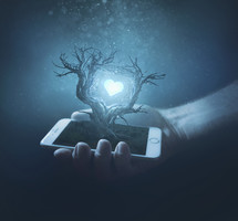 Holding a cell phone with a tree rising from the screen and glowing heart