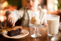 A boy in a restaurant enjoying chocolate cake, milk and ice cream.