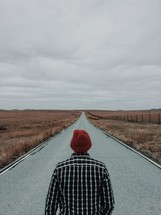 a man standing in the middle of a road looking at the road ahead 