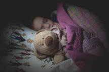 a child sleeping in bed with her teddy bear 