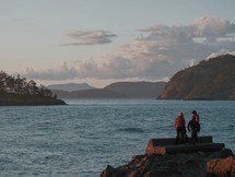 people standing on a rocky shore looking out at the water 