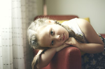little girl in pig tails with her head leaning on an arm of a chair