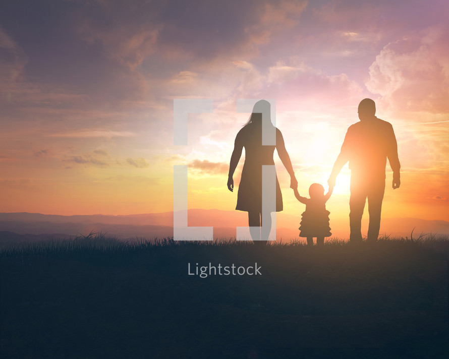 silhouette of a mother and father holding their daughters hand at sunset 