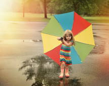 a little girl in rain boots carrying an umbrella 