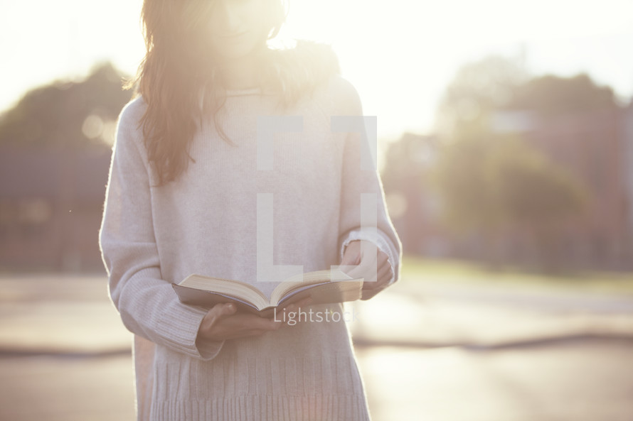 Teenage girl reading a Bible with a soft sun flare.