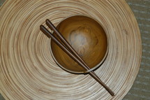 chop sticks resting on a wooden bowl on a bamboo mat
