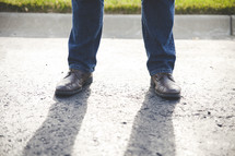 A man's legs standing on a sidewalk.
