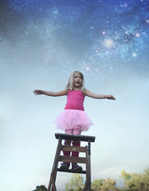 a little girl in a tutu standing on a ladder under the stars 